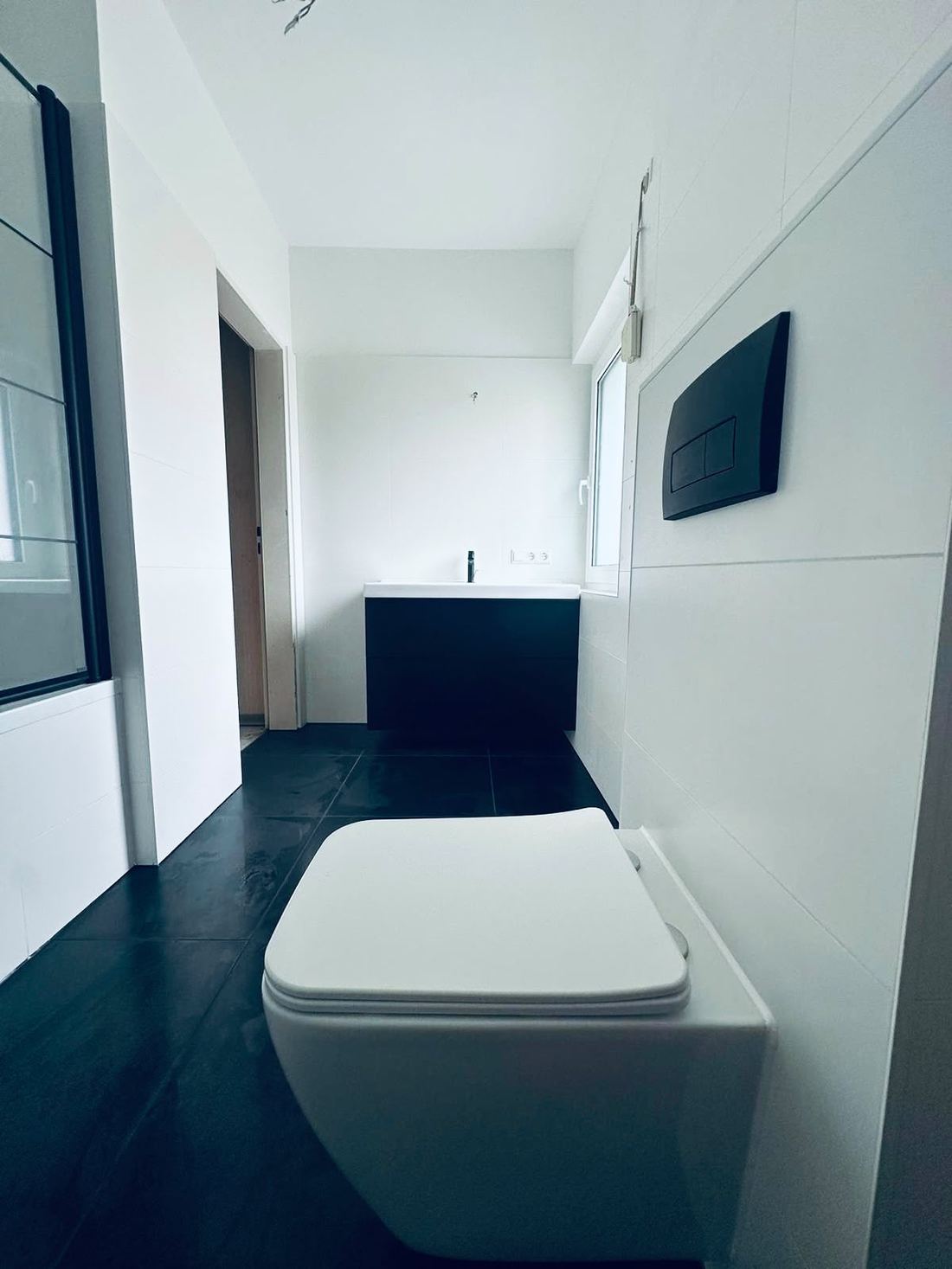 WC podwieszane i czarna szafka z umywalką w łazience z ciemną podłogą
